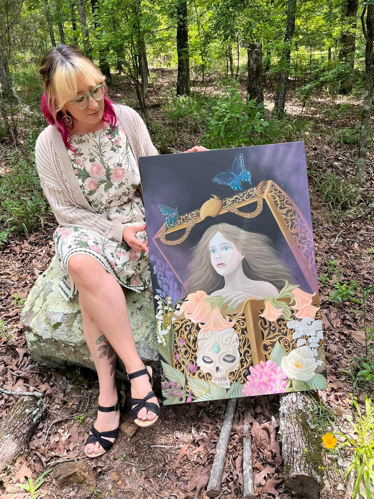 Kammie Reed sitting in the woods with one of her original oil paintings